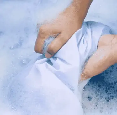 Pessoa lavando roupa com sabão em pó para obter uma limpeza eficaz, destacando a importância do melhor sabão em pó para remover manchas e deixar as roupas limpas.